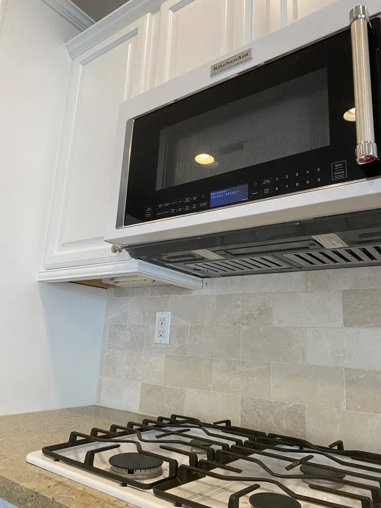 Over-the-range microwave installed above a new marble-look tile backsplash and gas cooktop